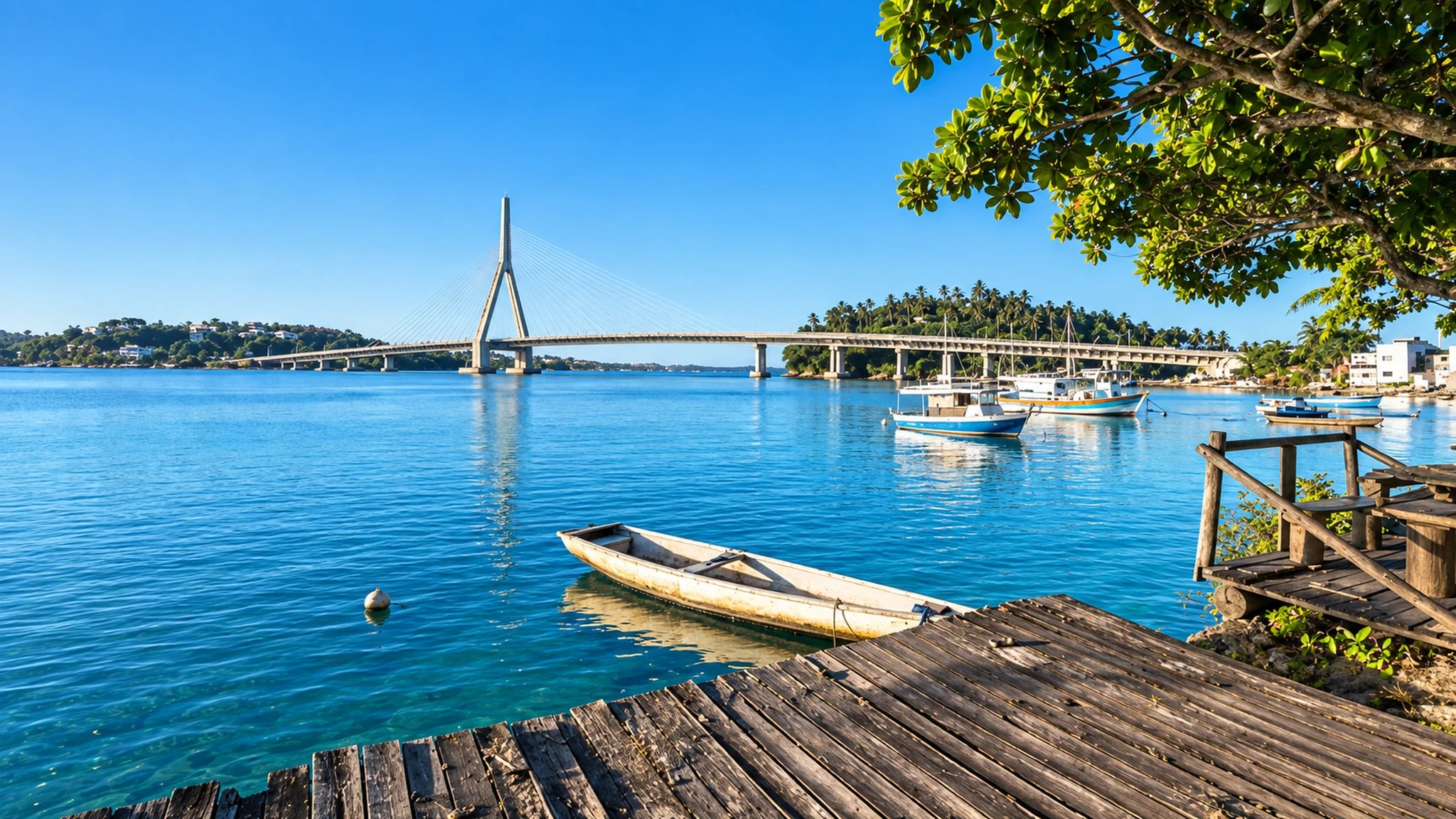 Baía com canoa, veleiros e ponte estaiada sob céu azul